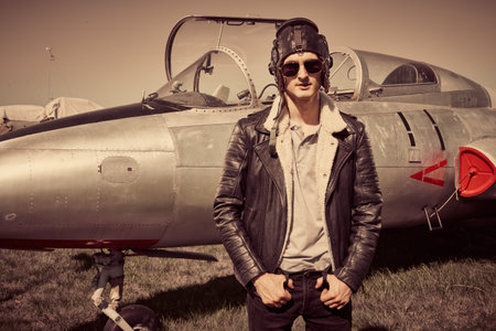 Handsome man pilot wearing helmet and leather jacket stands next to his  fighter jet. Military...