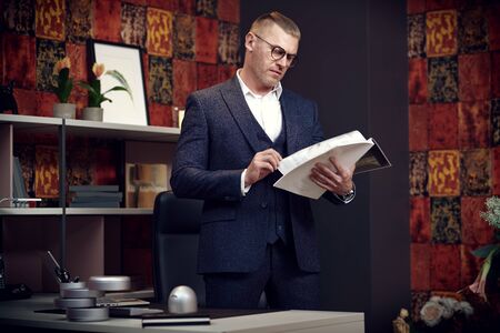 Serious middle-aged businessman in a suit and glasses works in a modern office. Successful manager concept.の写真素材