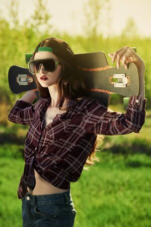 Cool modern teen girl posing with her longboard in the park. The spirit freedom and summer adventures.の写真素材