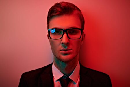 Men's fashion. Portrait of a handsome young businessman in a formal suit and glasses in red light. Business man studio portrait.の写真素材