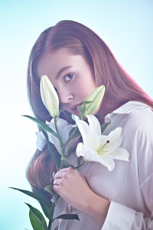 Beautiful young tender girl with lily flowers in a light pink-blue haze. Inspiration of spring and summer. Perfume, cosmetics concept.の写真素材