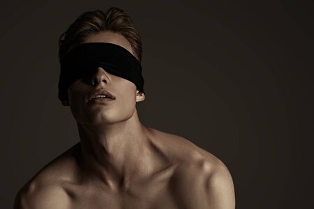 Art portrait of a handsome athletic young blindfold man with perfect muscular body. Sports and bodybuilding. Men's beauty and health. Copy space.の写真素材