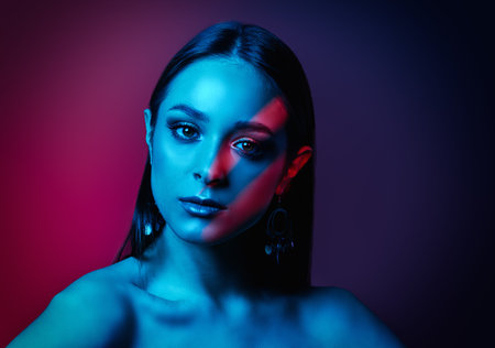 Beauty, Fashion concept. Portrait of an attractive brunette girl posing in color mixed light. Makeup and cosmetics, jewelry. Studio shot.の写真素材
