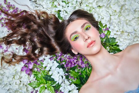 Spring beauty. Close up portrait of a tender girl with bright make-up and her eyes closed lying on a floral background. Make-up and cosmetics. Copy space.の写真素材