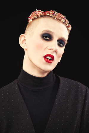 Portrait of a pale young man with womenâ€™s makeup and with red jewelry flower crown on the...