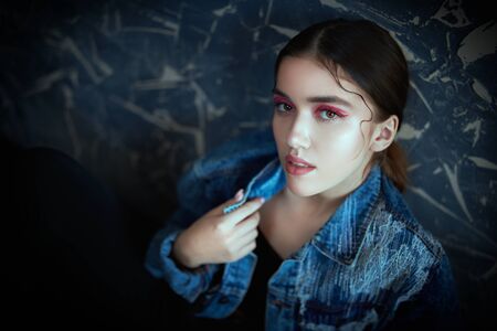 Fashion, beauty concept. Beautiful brunette girl posing in black clothes and jeans jacket at studio. Trendy shiny make-up with red arrows, cosmetics.の写真素材