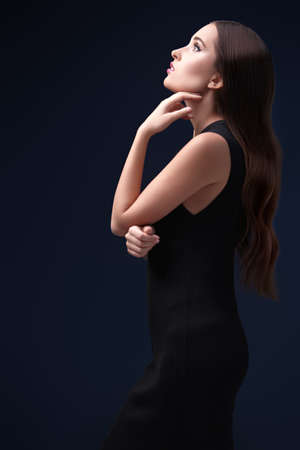 Fashion, beauty concept. Portrait of a gorgeous young woman in a tight black dress posing on a dark blue background. Copy space.の写真素材