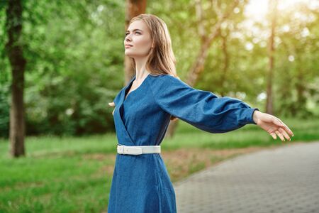 Portrait of a beautiful happy girl standing in the park, arms outstretched to the sides with happiness. Summer holidays.の写真素材