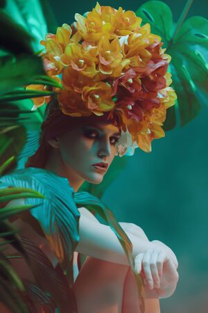 Fashionable female model posing among tropical plants in a beautiful orchid headgear. Beauty and fashion concept. Tropical vacation.の写真素材