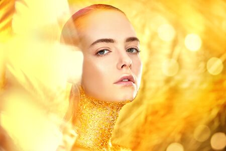 Beauty, fashion gold concept. Portrait of a beautiful girl model with golden skin and golden make-up on a sparkling background with golden lights. Jewelry. Cosmetics and beauty care. Copy space.の写真素材
