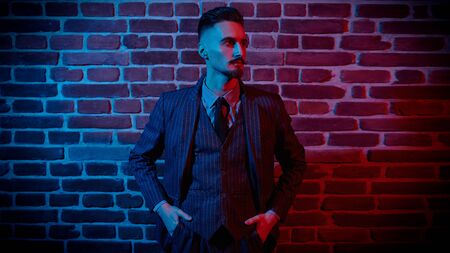 Portrait of a handsome young man in elegant suit standing in red light by a brick wall. Men's fashion. Luxurious lifestyle.の写真素材