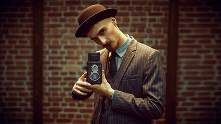 Retro concept. Handsome photographer man in an elegant suit is working with his old camera on a brick wall background.の写真素材