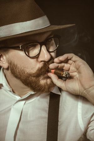 A close up portrait of a thoughtful man with a cigar posing in the studio over the black background....