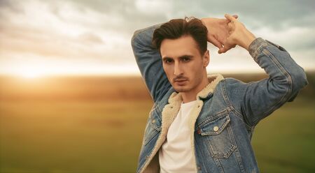 Portrait of a handsome young man in jeans jacket on the background of the green valley. Male beauty, denim style.の写真素材