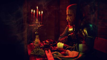 An experienced medieval warrior in armor and with a sword in a wooden house. Stage portrait. The Witcher man.の写真素材