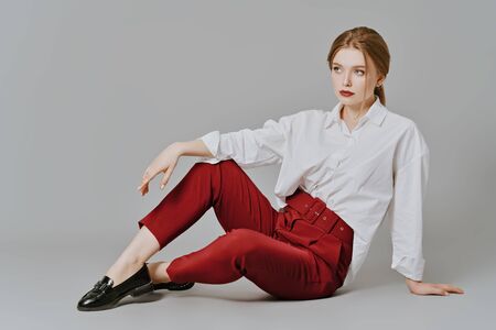 Beauty, fashion portrait. Elegant business style. Full length portrait of a beautiful blonde woman in white blouse and red pants posing at studio on a gray background.の写真素材