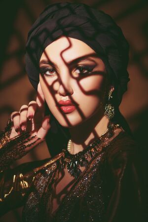 Oriental fairy tale. Portrait of a beautiful arab woman with traditional make-up and black hijab. Make-up and cosmetics.の写真素材