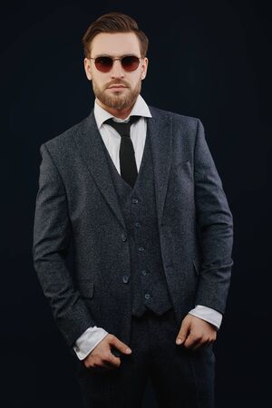 Portrait of a handsome smiling man wearing suit and sunglasses on a black background. Businessman portrait. Men's beauty, fashion. Optics for men.の写真素材