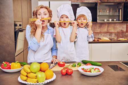 Happy family concept. Funny children and their mother make a mustache of spaghetti and cook dinner. Healthy eating.の写真素材