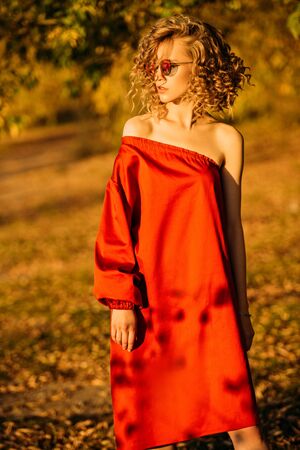 A beautiful young girl is posing in the countryside in a red dress. Fashion concept. Golden autumn.の写真素材