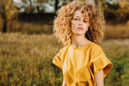 A portrait of a charming young girl with curly fair hair in a yellow dress. Fashion, beauty.の写真素材