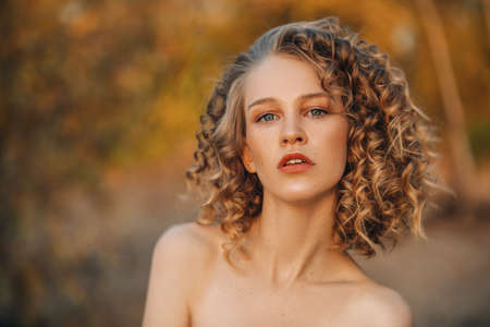 A close-up portrait of a pretty young girl with curlt hair posing outside in nature. Skincare, health, beauty.の写真素材