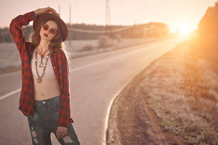 Cool modern teen girl posing on a highway outside the city on a sunset. The spirit freedom and summer adventures.の写真素材