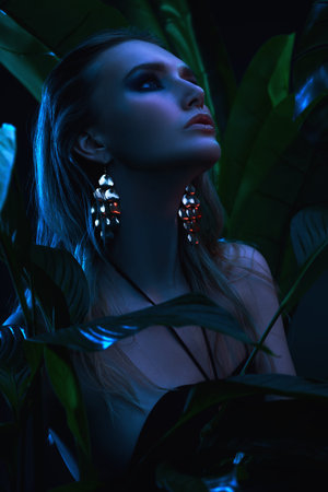 Portrait of a beautiful tropical woman with wet hair standing among palm leaves. Beauty, fashion and...