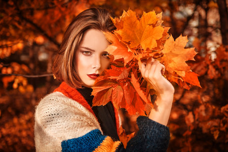 Beautiful romantic girl with a bouquet of maple leaves at the autumn park. Autumn beauty, fashion.