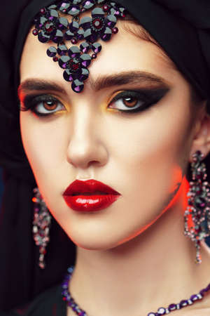 Arabian beauty, fashion. Close up portrait of a beautiful oriental woman with traditional make-up, black hijab and jewelry on a black background. Make-up and cosmetics.の写真素材