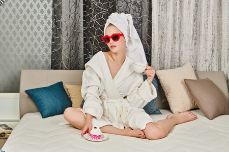 Glamorous young woman in elegant sunglasses, a white bathrobe and with a towel around her hair after...