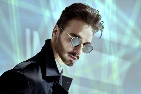 Modern stylish man in elegant black coat and sunglasses posing on a grey background with shadows. Portrait of a modern businessman. Men's fashion.の写真素材