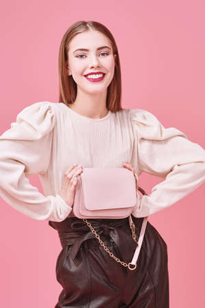 Fashionable young woman posing at studio in modern clothes and sunglasses on a pink background.の写真素材