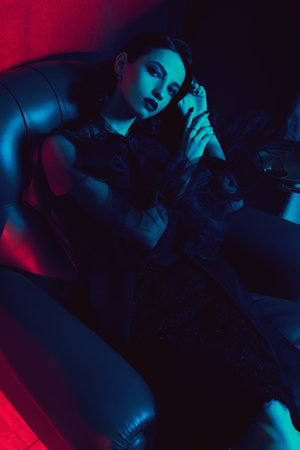 Portrait of a beautiful brunette young woman in fashionable black clothes sitting in a leather...