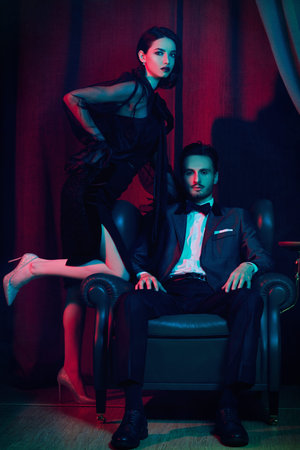 Beautiful elegant couple in fashionable evening clothes posing in a luxury apartment. Glamorous...