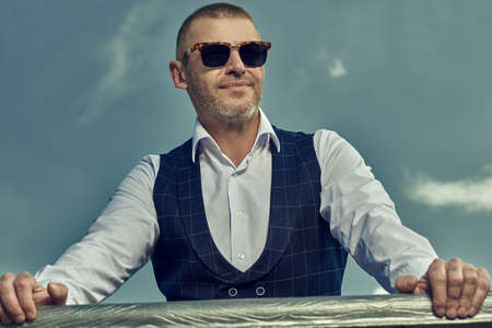 Portrait of a handsome mature man in an elegant classic suit standing. Male beauty, fashion. Optics, sunglasses for men.の写真素材