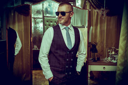 Portrait of a handsome mature man in an elegant classic suit standing in a luxury apartment. Male beauty, fashion. Optics, sunglasses for men.の写真素材
