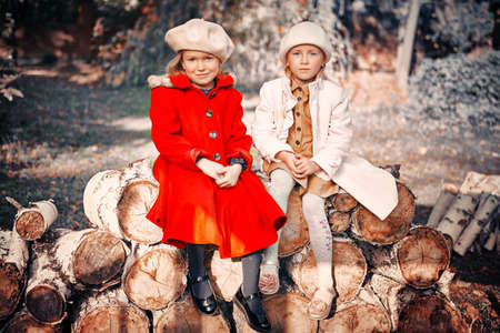 Two cute little girls sit together in a beautiful autumn park. Retro style. Children's fashion.の写真素材