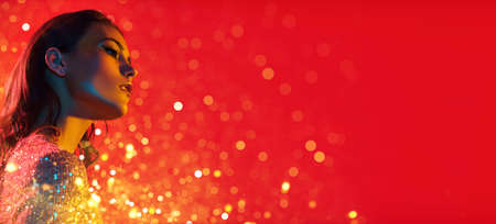 Make-up and cosmetics. Portrait of a gorgeous young woman with golden make-up in a colored red, blue and yellow light on a red background. Party style. Copy space.の写真素材