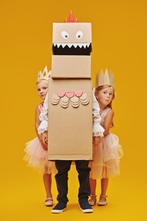 Funny little girls hiding behind a cardboard dragon, dinosaur. Childhood dreams. Fantasy,...