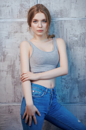 Portrait of a beautiful slim girl in jeans and a sports top against a grunge wall. Active lifestyle....