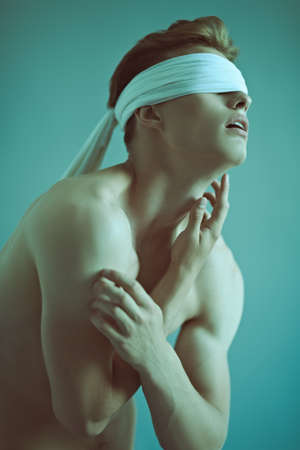 Art portrait of a handsome blindfold young man with perfect muscular body. Sports and bodybuilding. Men's beauty and health. Copy space.の写真素材