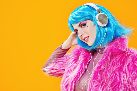 Attractive party girl with bright pink makeup and blue wig wearing pink fur coat and headphones on a...