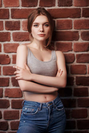 Portrait of a beautiful smiling girl in jeans and a sports top against a brick wall. Active lifestyle. Beauty, fashion.の写真素材