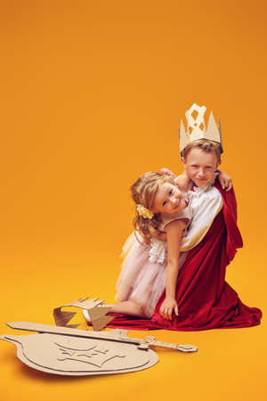 A boy and a girl in Prince and Princess costumes laugh and hug. Childhood dreams. Fantasy, imagination. Studio portrait on a yellow background.の写真素材