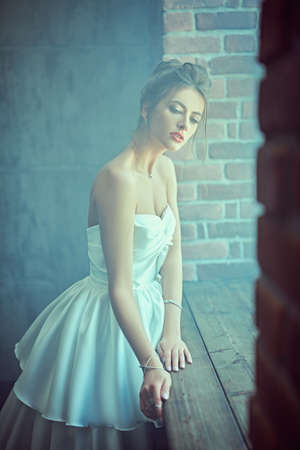 Full length portrait of a beautiful fashion model in a luxury wedding dress posing at studio on a grunge background near a window. Wedding fashion.の写真素材