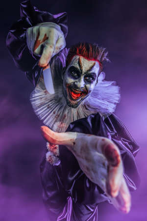 A portrait of an angry crazy clown from a horror film holding a table knife. Halloween, carnival.の写真素材