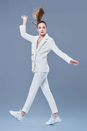 Fashion shot. Portrait of a beautiful young woman in a white suit jumping running on a gray background. Trendy makeup with blue aquamarine eye arrows. Make-up and cosmetics.の写真素材