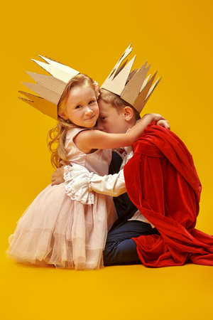 Funny boy and girl in Prince and Princess costumes are hugging. Childhood dreams. Fantasy, imagination. Studio portrait on a yellow background.の写真素材