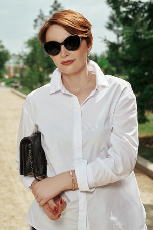 Portrait of a modern middle-aged woman in sunglasses in the park on a summer day. Optics for women....